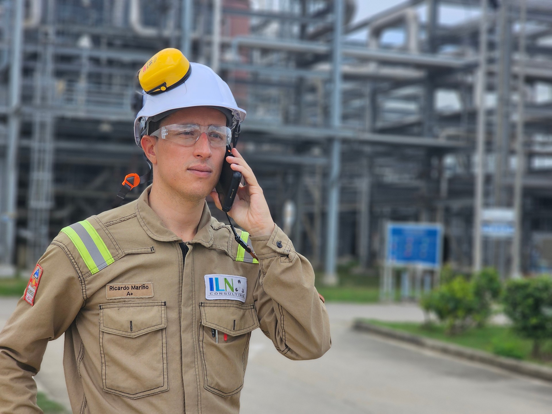 Profesional de ILN con casco y gafas de seguridad se comunica por teléfono en una instalación industrial
