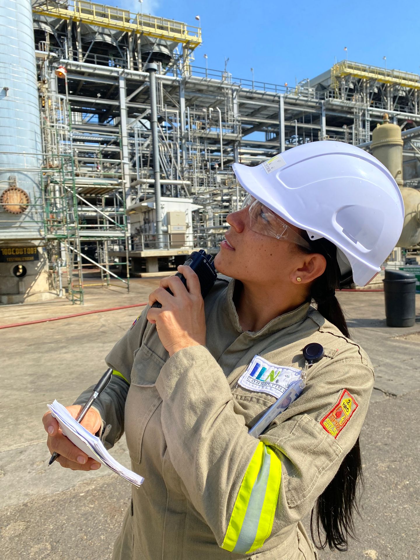 Profesional de ILN con casco utiliza un radio y una libreta en una instalación industrial