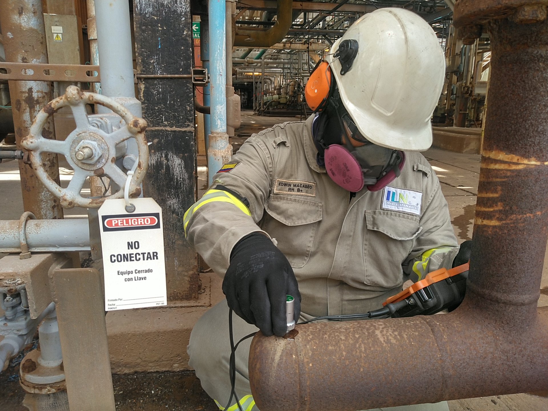 Profesional de ILN registra información junto a una válvula y tuberías industriales