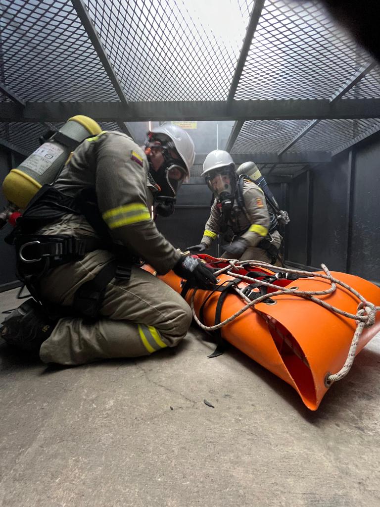 Dos integrantes de un equipo de rescate con protección respiratoria preparan una camilla y cuerdas en un entorno industrial